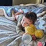 toddler, child, baby_bottle, blanket, bed, plush_toy, stuffed_animal, yellow_chicks, soft_toys, indoor, cozy, curly_hair, laying_down, cute, young_child, comfort, resting, playful, home, nap_time