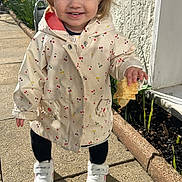 Juliette a rejoint le concours — aidez-le/la à gagner de superbes lots ! child, toddler, smiling, jacket, cherry_pattern, sneakers, sidewalk, sunlight, shadow, flowerbed, wall, plant, hand, food, hairclip, face, outdoor, standing, coat, cup
