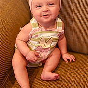 Delilah joined the competition — help win amazing prizes! baby, child, smiling, headband, pink, striped_clothing, bunny_design, sitting, couch, brown_couch, happy, indoors, infant, cute, portrait, person, skin, legs, feet, hand