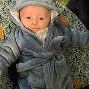 Isaac is registered to the contest to win money with this photo: baby, blue_robe, hood, face, infant, smiling, pillow, patterned, bottle, feeding_bottle, soft_clothing, cute, indoors, child, young, cozy, person, apparel, sleepwear, lying_down