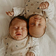 Louise Et Lola participe au concours pour gagner de l'argent avec cette photo : baby, infant, newborn, two_babies, lying_down, white_blanket, matching_outfits, beige_clothing, floral_pattern, smiling, peaceful, cute, sleepy, portrait, soft_lighting, indoor, closeup, child, head, hands