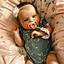 Kyah Kay is registered to the contest to win money with this photo: baby, pacifier, headband, floral_pattern, cushion, soft_texture, infant, clothing, green_outfit, lying_down, closeup, skin, hand, face, expression, cute, comfort, indoors, portrait, child