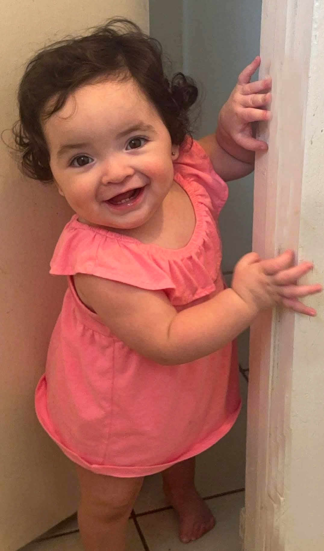 Alyana Rocha joined the competition — help win amazing prizes! toddler, child, smiling, curly_hair, pink_dress, barefoot, door_frame, indoor, happy, cute, baby, person, skin, face, hand, foot, standing, portrait, young_child, expression