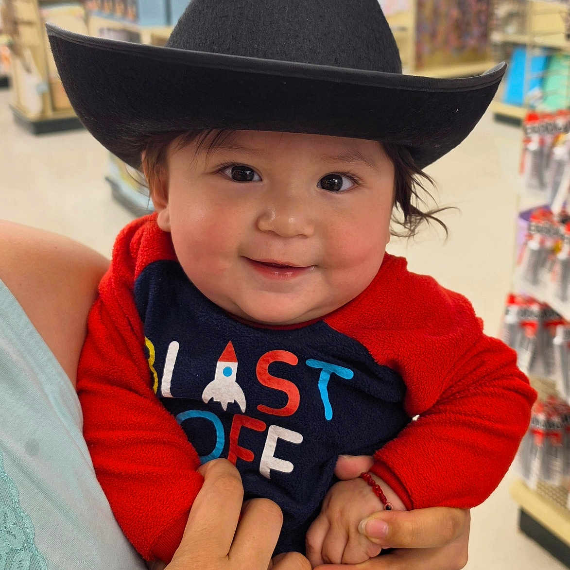 Alexander joined the competition — help win amazing prizes! baby, child, cowboy_hat, smile, red_clothing, onesie, person, indoor, store, aisle, hand, holding, cute, face, young_child, toy_store, colorful, clothing, happy, portrait
