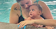 Andre joined the competition — help win amazing prizes! baby, woman, swimming_pool, water, tattoo, toy, child, person, swimsuit, playing, holding, curious, interaction, family, poolside, skin, wet, summer, fun, bonding