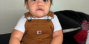 Lyett is registered to the contest to win money with this photo: baby, bed, blanket, brown_clothing, child, colorful_clips, expression, face, hair_ties, hands, indoor, jar, overalls, person, pigtails, pillow, sitting, toddler, white_shirt, young_child