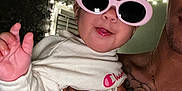 Lyett is registered to the contest to win money with this photo: baby, child, sunglasses, pink_sunglasses, tattoo, tattooed_arm, hand, smile, tongue_out, indoor, string_lights, adult, person, closeup, portrait, casual, fun, cute, fashion, white_shirt