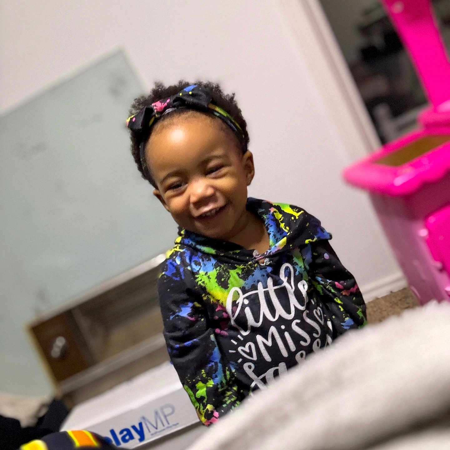 Zaphoria is registered to the contest to win money with this photo: blanket, carpet, casual, child, colorful_clothing, cute, expression, furniture, happy, headband, home, hoodie, indoor, person, playroom, portrait, smiling, toddler, toy, young_child