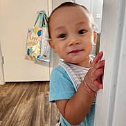 Kyle joined the competition — help win amazing prizes! baby, child, toddler, face, portrait, peeking, curious, indoors, doorway, door_frame, hands, smiling, eyes, short_hair, blue_shirt, striped_clothing, hallway, wood_floor, home, photography