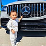 Kyle joined the competition — help win amazing prizes! child, toddler, smiling, outdoor, car, suv, mercedes, vehicle, grille, logo, automobile, sunlight, blue_sky, driveway, standing, portrait, fashion, bib, white_clothing, family_photo