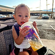 Kyle is registered to the contest to win money with this photo: baby, casual, child, clothing, cloud, drink, face, hand, outdoor, palm_tree, parking_lot, person, plastic_cup, seat, sky, straw, stroller, sunset, toddler, vehicle