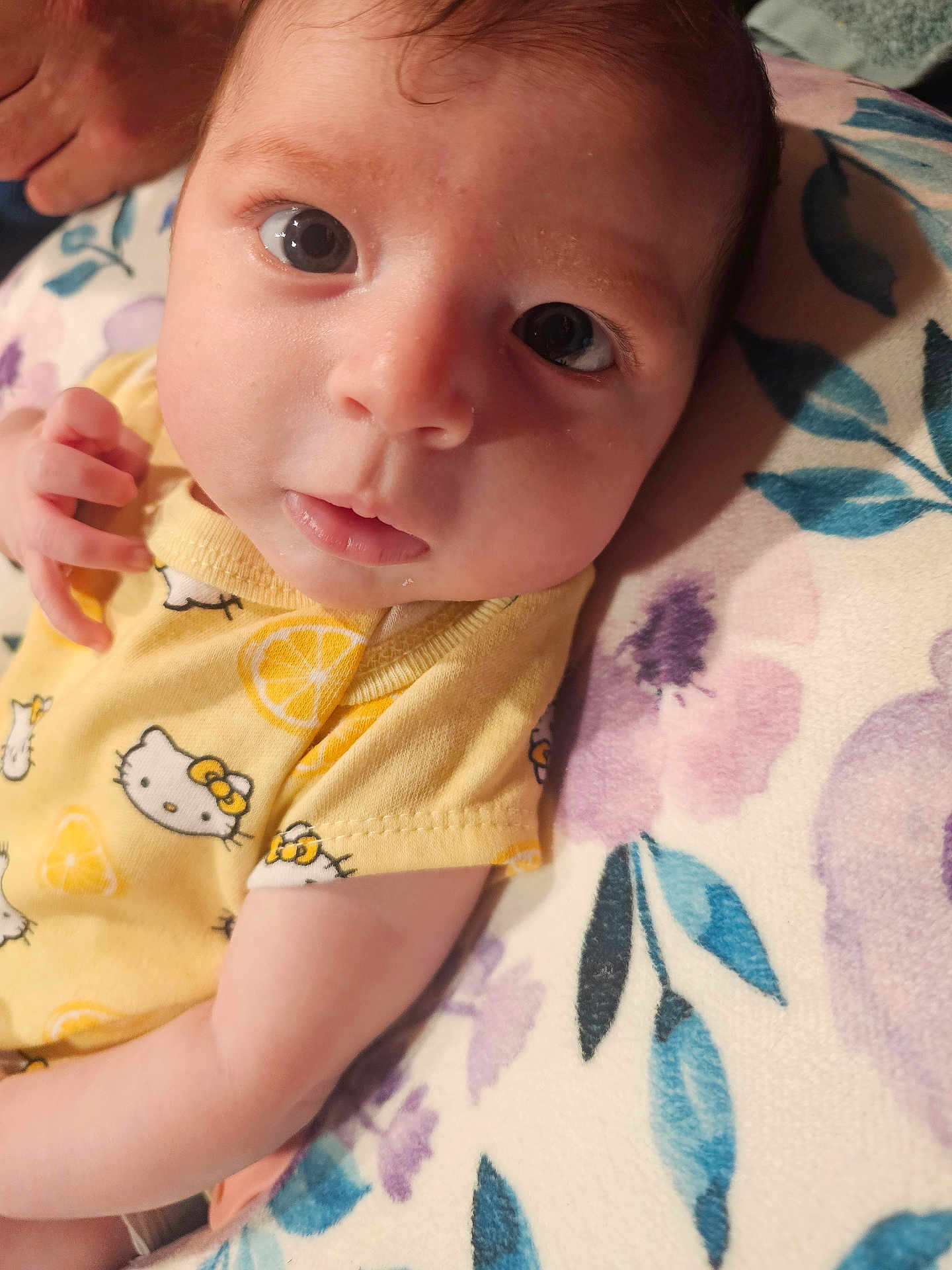Isabella is registered to the contest to win money with this photo: baby, infant, face, eyes, yellow_clothing, hello_kitty, onesie, hand, blanket, floral_pattern, cute, portrait, newborn, skin, person, lying_down, soft_texture, indoors, closeup, child