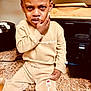 child, tearful, distressed, beige_clothing, tracksuit, kitchen, counter, appliance, sitting, face, hand, sweatshirt, pants, expression, indoor, person, young_child, clothing_brand, emotional, portrait