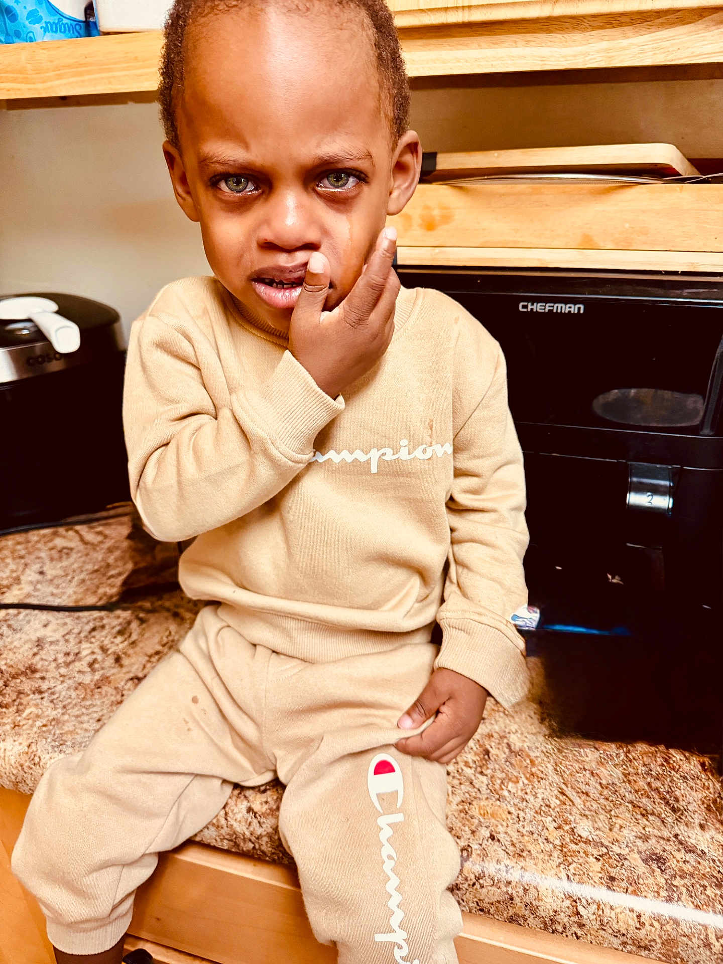 Matthew joined the competition — help win amazing prizes! child, tearful, distressed, beige_clothing, tracksuit, kitchen, counter, appliance, sitting, face, hand, sweatshirt, pants, expression, indoor, person, young_child, clothing_brand, emotional, portrait