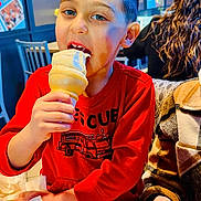 Gio joined the competition — help win amazing prizes! child, boy, ice_cream, cone, eating, smiling, restaurant, indoor, portrait, red_shirt, sweatshirt, fire_truck, table, food, dessert, seated, phone, adult, background, photograph