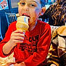child, boy, ice_cream, cone, eating, smiling, restaurant, indoor, portrait, red_shirt, sweatshirt, fire_truck, table, food, dessert, seated, phone, adult, background, photograph