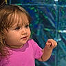 child, toddler, baby, girl, portrait, pink_shirt, brown_hair, blue_eyes, curious, looking_sideways, indoor, colorful_background, sparkles, bokeh, closeup, sitting, hand, reaching, face, safe