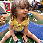 Sofia is registered to the contest to win money with this photo: toddler, child, smiling, portrait, indoor, playroom, toy, turtle, ride_on_toy, yellow_shirt, brown_hair, blue_eyes, sitting, happy, carpet, colorful, family, recreation, playground, photography
