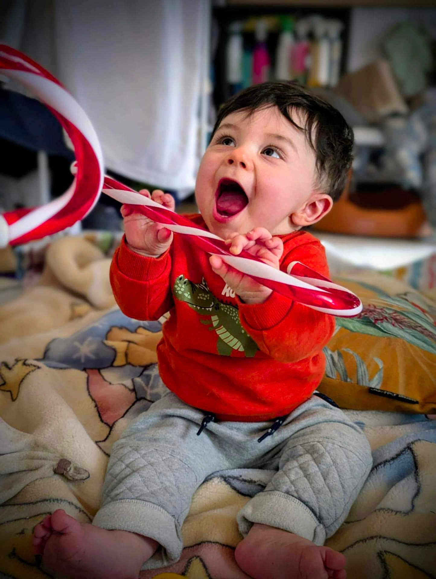 Djeïck participe au concours pour gagner de l'argent avec cette photo : baby, child, candy_cane, orange_sweater, dinosaur_print, blanket, sitting, happy, excited, indoors, cozy, cute, feet, hands, portrait, smiling, young_child, playful, comfort, closeup