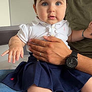 Nélya participe au concours pour gagner de l'argent avec cette photo : baby, child, man, holding, watch, hand, face, blue_eyes, hair_clip, white_shirt, navy_skirt, jeans, sitting, indoor, person, parent, family, curious, cute, portrait
