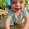 baby, blue_bowl, cardboard_box, child, closeup, cute, daylight, deck, expression, greenery, happy, infant, outdoor, person, playful, short_sleeve_shirt, smiling, sunny, wooden_floor, young