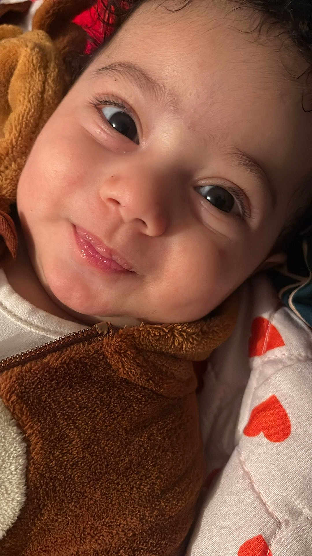Youssef Adda participe au concours pour gagner de l'argent avec cette photo : baby, close_up, smile, face, eyes, fuzzy_jacket, brown, white_shirt, pillow, red_hearts, infant, cute, skin, child, young, lying_down, cozy, expression, indoors, warm