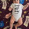 Joel is registered to the contest to win money with this photo: baby, infant, onesie, blanket, harry_potter, child, smiling, cute, lying_down, clothing, face, skin, arms, legs, happy, person, text_on_clothing, patterned_blanket, indoor, portrait