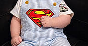 Joel joined the competition — help win amazing prizes! baby, smiling, superman_logo, overalls, striped_clothing, cute, chubby, sitting, leather_couch, happy, child, portrait, indoor, infant, shorts, button, tshirt, curly_hair, skin, furniture
