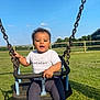 toddler, child, swing, playground, outdoor, grass, blue_sky, clouds, sunny, givenchy, white_tshirt, mismatched_socks, happy, holding, metal_chains, fence, park, casual_clothing, daylight, smiling