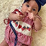 Millie is registered to the contest to win money with this photo: baby, child, infant, headband, bow, beads, red, white, blue, checkered, clothing, face, hand, soft_surface, curious, portrait, cute, lying_down, indoor, person