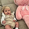baby, infant, teddy_bear, plush_toy, sofa, couch, headband, clothing, sitting, smile, cute, indoor, person, soft_toy, white_socks, knitwear, child, portrait, furniture, cozy