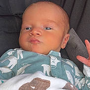 William is registered to the contest to win money with this photo: baby, infant, blanket, onesie, clothing, face, portrait, child, newborn, cute, skin, hand, expression, blue_eyes, sleepwear, indoors, closeup, cozy, resting, serious