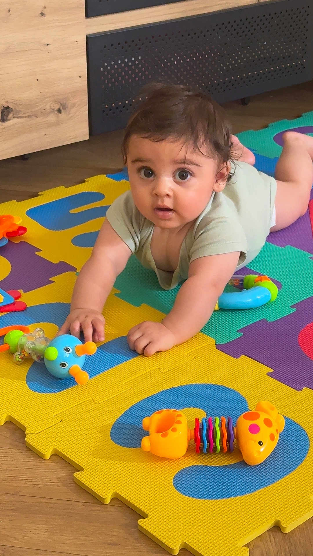 Emilio participe au concours pour gagner de l'argent avec cette photo : baby, child, toy, colorful, foam_mat, floor, wooden_floor, indoor, playtime, curious, infant, crawling, cute, person, small_toy, plastic_toy, bright_colors, mat, expression, home