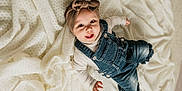 Odayah joined the competition — help win amazing prizes! baby, child, infant, denim_overalls, headband, bow, smiling, happy, lying_down, blanket, white_blanket, cute, clothing, portrait, one_person, indoors, baby_hand, baby_face, soft_texture, cozy