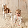 baby, infant, crawling, white_clothing, plush_toy, teddy_bear, chair, fluffy_rug, wooden_wall, indoors, child, cute, portrait, soft_lighting, cozy, floor, expression, young_child, looking_up, person