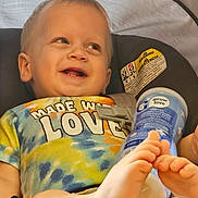 Micah joined the competition — help win amazing prizes! toddler, child, car_seat, tie_dye_shirt, smiling, feet, blue_container, baby, happy, infant, clothing, seatbelt, closeup, portrait, cute, foot, expression, indoor, holding, colorful