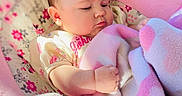 Lydia is registered to the contest to win money with this photo: baby, infant, blanket, pink, floral_pattern, baby_seat, clothing, fist, face, cheeks, soft_toys, indoor, portrait, cute, newborn, person, child, expression, warm, comfortable
