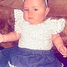 Lydia is registered to the contest to win money with this photo: baby, child, face, sunglasses, clothing, dress, skirt, pillow, couch, indoor, portrait, cute, fashion, serious, person, infant, sitting, white, blue, decor