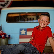 Rhett is registered to the contest to win money with this photo: americanflag, bodypart, boy, child, clothing, face, finger, flag, hand, happy, head, jeans, male, pants, person, photography, portrait, shorts, sitting, smile