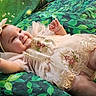 baby, child, smile, dress, headband, embroidery, lace, green_background, leaf_pattern, infant, cute, happy, portrait, toddler, soft_fabric, reaching_hand, lying_down, closeup, person, indoors