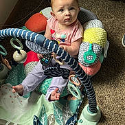 Lyric is registered to the contest to win money with this photo: baby, child, infant, play_seat, toy, carpet, cable, patterned_fabric, indoor, curious, looking_up, colorful, soft_toys, footwear_absent, striped_pants, pink_shirt, play_area, floor, home, person