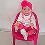 baby, infant, child, smiling, pink_headband, flower_headband, pink_chair, plastic_chair, bib, pink_pants, socks, white_wall, tile_floor, indoor, portrait, cute, happy, reaching, one_person, toddler