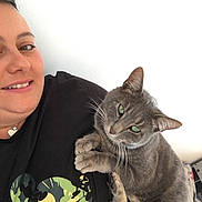 Oziris participe au concours pour gagner de l'argent avec cette photo : person, cat, smiling, cuddling, gray_cat, green_eyes, indoor, casual, portrait, close_up, black_shirt, mickey_mouse_print, short_hair, light_skin, white_background, pet, friendly, relaxed, feline, happy