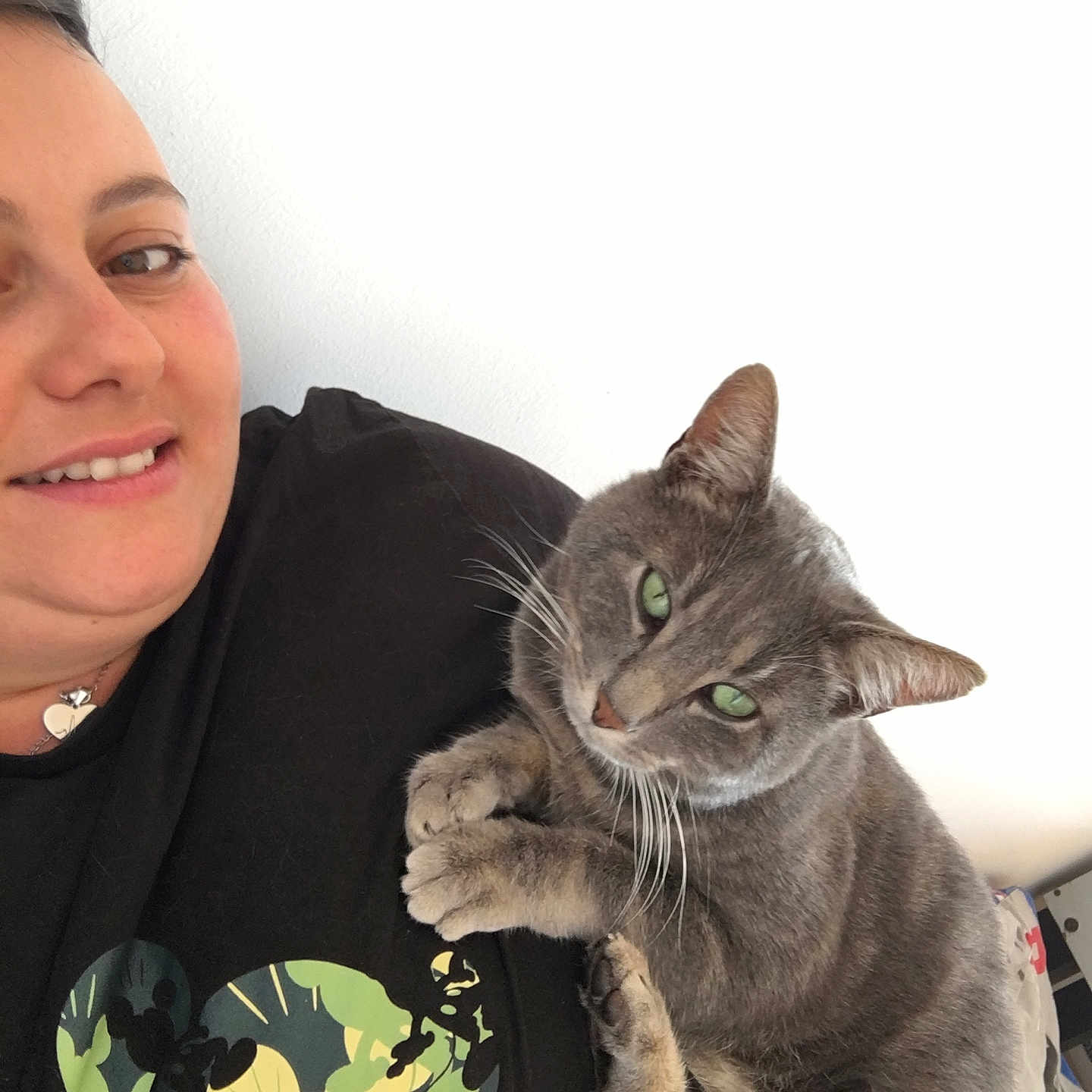 Oziris participe au concours pour gagner de l'argent avec cette photo : black_shirt, casual, cat, close_up, cuddling, feline, friendly, gray_cat, green_eyes, happy, indoor, light_skin, mickey_mouse_print, person, pet, portrait, relaxed, short_hair, smiling, white_background