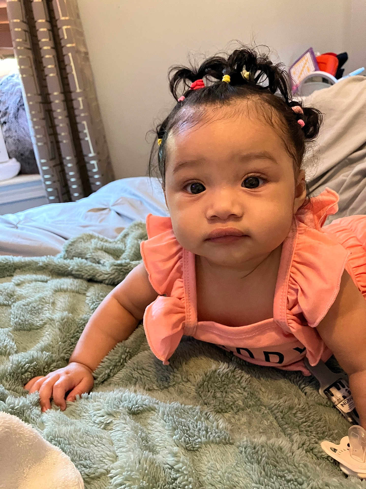 Yazlyn joined the competition — help win amazing prizes! baby, child, infant, cute, pigtails, colorful_hair_bands, blanket, indoor, bedroom, curtains, soft_texture, pink_clothing, expression, face, portrait, lying_down, hand, cozy, homely, pacifier