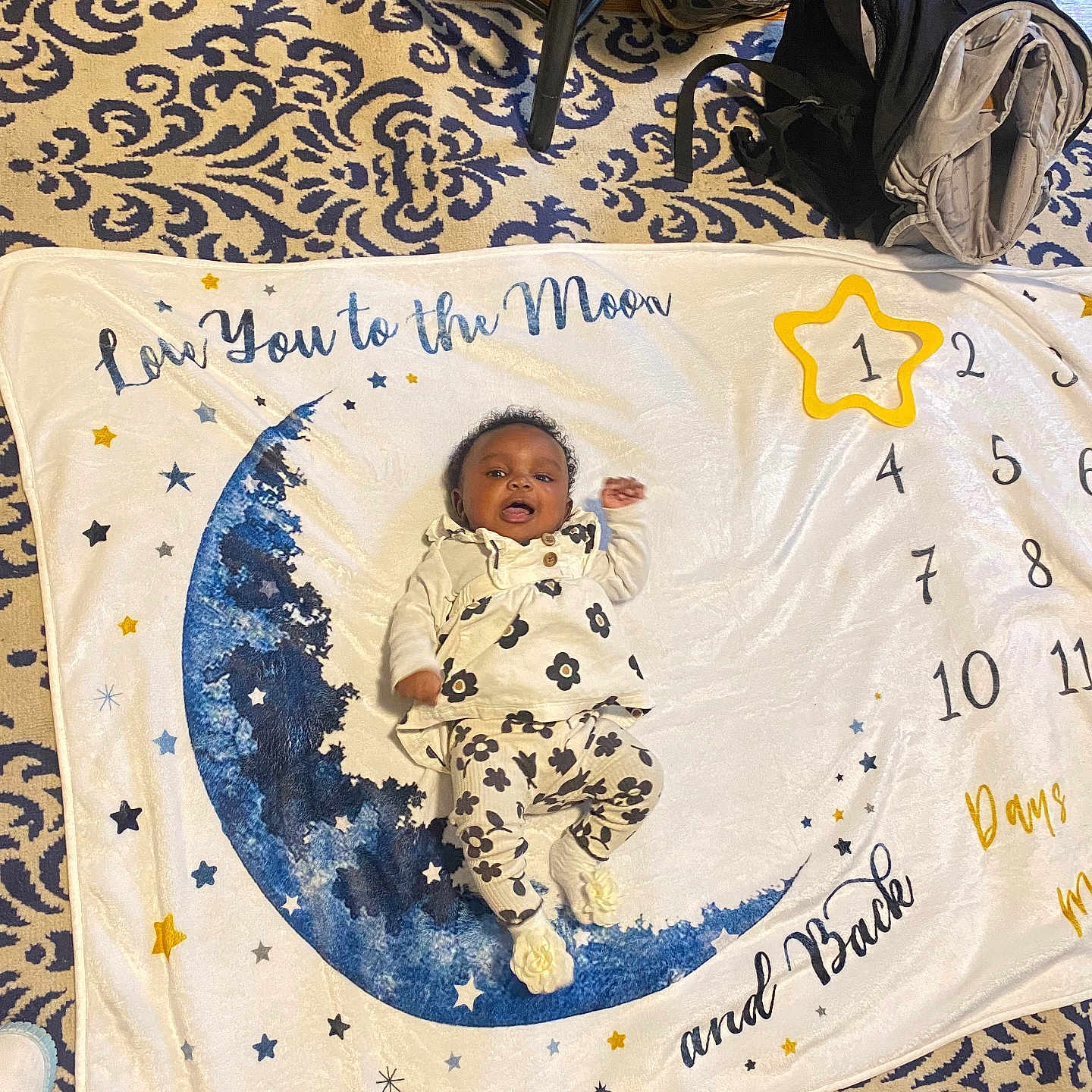Azaya joined the competition — help win amazing prizes! baby, backpack, blanket, child, clothing, cute, decor, floor, floral_outfit, footwear, home, indoor, infant, milestone_blanket, moon, patterned_rug, person, smiling, stars, toy
