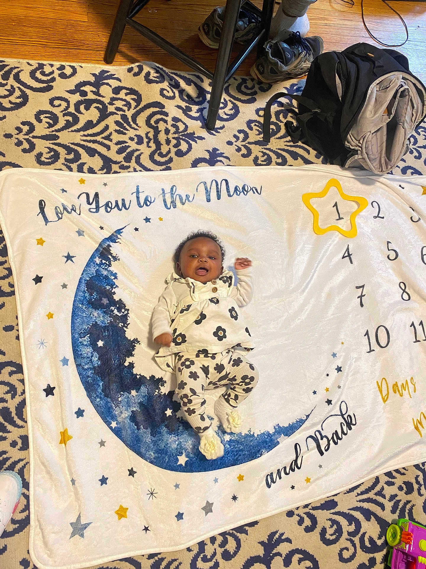 Azaya joined the competition — help win amazing prizes! baby, infant, milestone_blanket, moon, stars, patterned_rug, floral_outfit, footwear, backpack, toy, floor, indoor, child, smiling, clothing, blanket, decor, home, person, cute