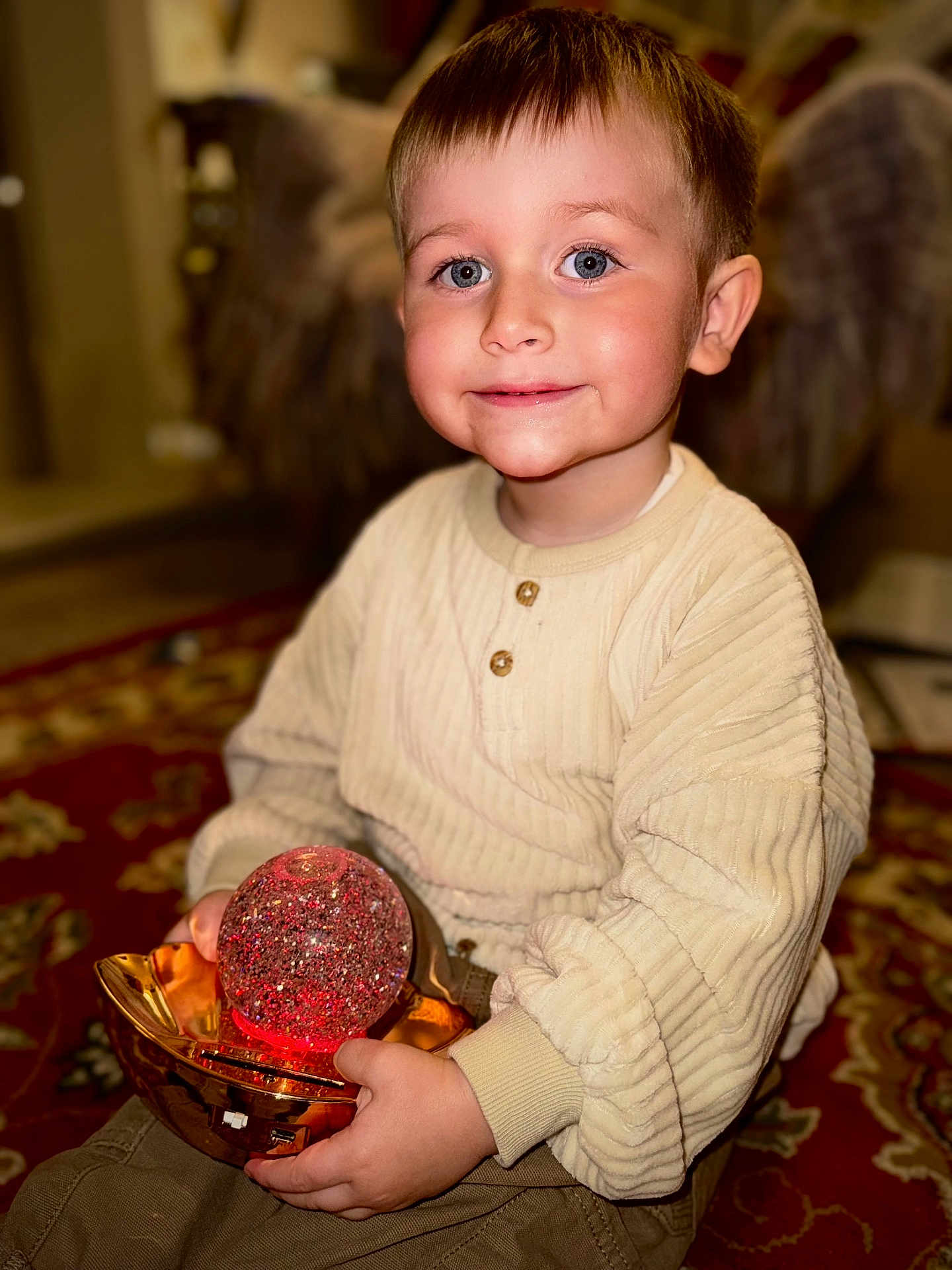 Kayson is registered to the contest to win money with this photo: child, boy, indoor, carpet, toy, glowing, orb, golden_holder, smiling, blue_eyes, rosy_cheeks, sweater, long_sleeves, hands, face, portrait, cute, cozy, home, playful