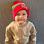 Kayson joined the competition — help win amazing prizes! child, toddler, beanie, red_hat, sweatshirt, pants, standing, indoor, portrait, face, smile, curious, young_child, clothing, casual, cozy, headwear, person, wall, texture