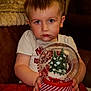 toddler, child, face, blue_eyes, snow_globe, christmas_tree, red_blanket, white_tshirt, indoor, cozy, couch, holiday, hands, portrait, expression, young_child, home, soft_lighting, closeup, person